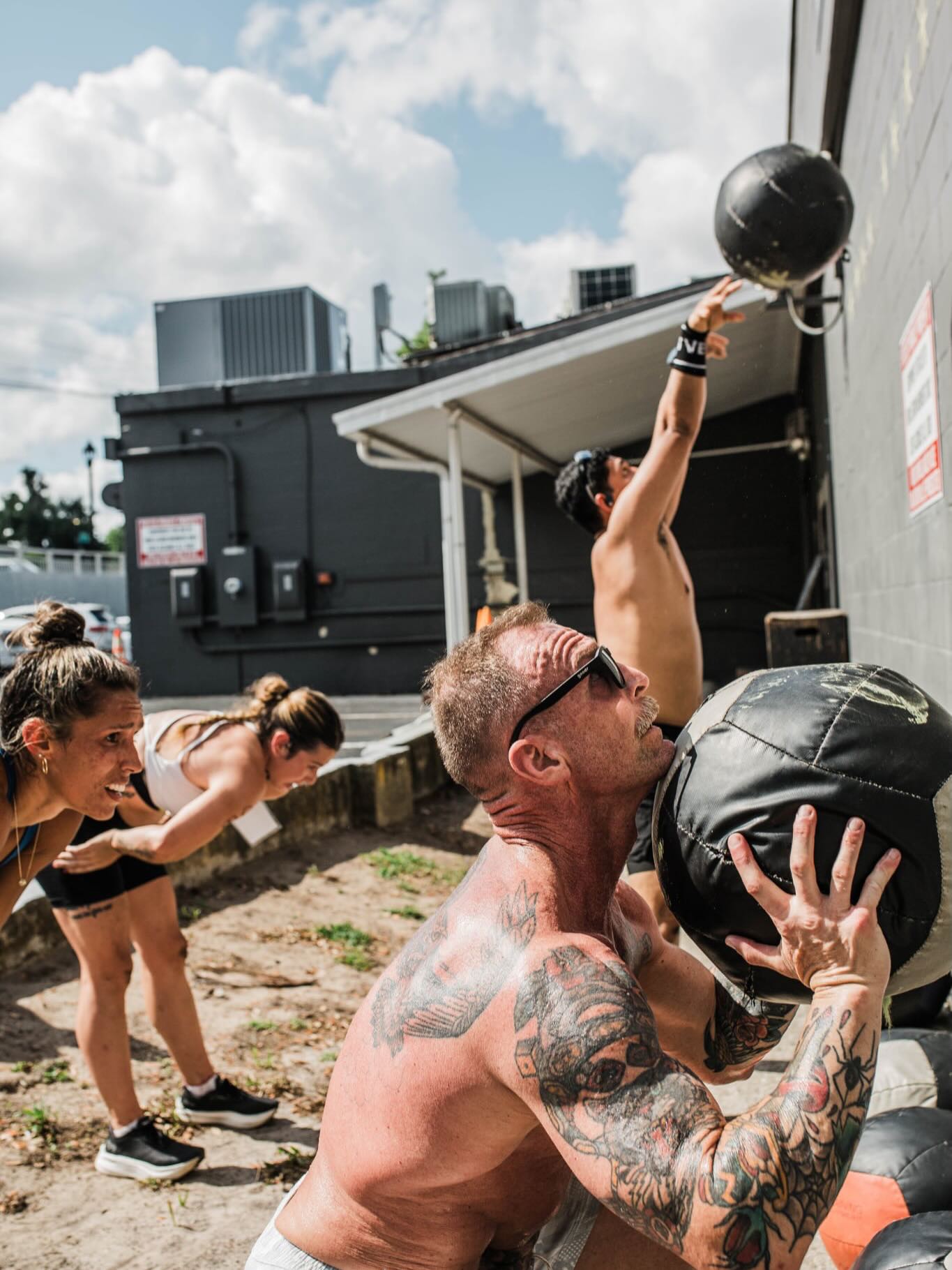 Male athlete with tattoos performing wall ball shots against a building wall during the Rox Race at Iron Legion